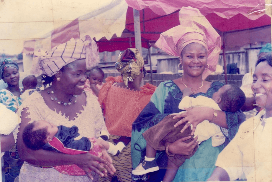 A smiling mother holding a baby while surrounded by community members outdoors